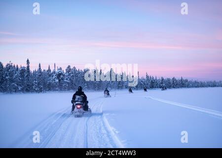 Escursioni in motoslitta sul lago ghiacciato al tramonto a Torassieppi, Lapponia, Finlandia Foto Stock