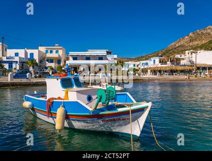 Finiki, Karpathos, Grecia - 16 settembre 2019: Colorata barca da pesca che galleggia su un'acqua con Finiki Waterfront con taverne e spiaggia Foto Stock