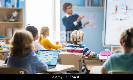 L'insegnante di fisica della scuola elementare usa la lavagna interattiva digitale per mostrare In un'aula piena di bambini intelligenti e diversificati come rinnovabili Energia funziona Foto Stock