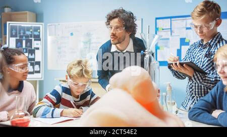 Scuola elementare chimica Classroom: Insegnante entusiasta insegna diversi gruppi di bambini mostra esperimento di reazione scientifica mescolando sostanze chimiche in Foto Stock