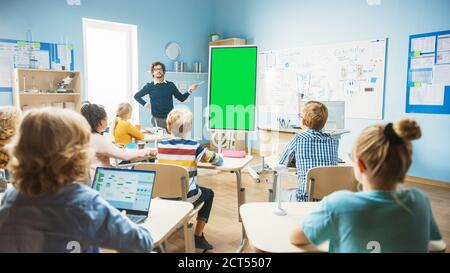 L'insegnante di fisica della scuola elementare usa la lavagna interattiva digitale con il modello di mock-up dello schermo verde. Conduce le lezioni in classe piena di intelligenza Foto Stock