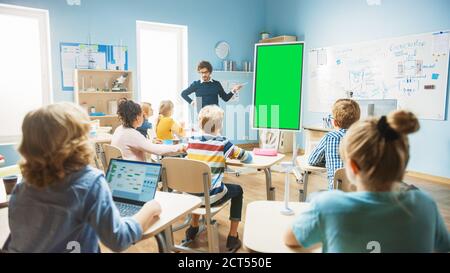 L'insegnante di fisica della scuola elementare usa la lavagna interattiva digitale con il modello di mock-up dello schermo verde. Conduce le lezioni in classe piena di intelligenza Foto Stock