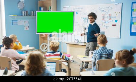 L'insegnante di fisica della scuola elementare usa la lavagna interattiva digitale con il modello di mock-up dello schermo verde. Conduce le lezioni in classe piena di intelligenza Foto Stock