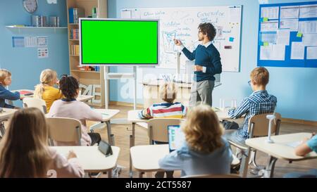 L'insegnante di fisica della scuola elementare usa la lavagna interattiva digitale con il modello di mock-up dello schermo verde. Conduce le lezioni in classe piena di intelligenza Foto Stock