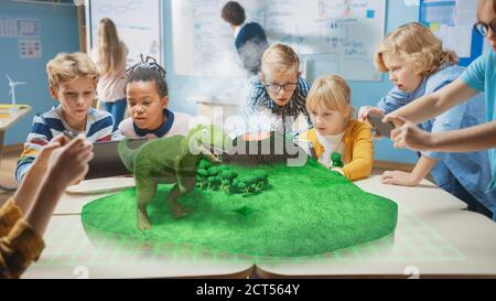 Gruppo di bambini della scuola usano i calcolatori digitali del tablet con l'applicazione di realtà aumentata, guardando l'animazione 3D educativa - camminata dei dinosauri sull'isola Foto Stock