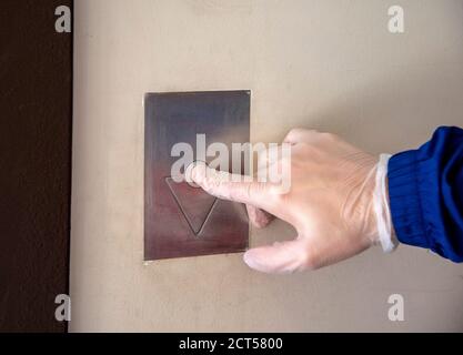 Una mano dell'uomo in un guanto di gomma, premendo il pulsante per chiamare l'ascensore. Foto Stock