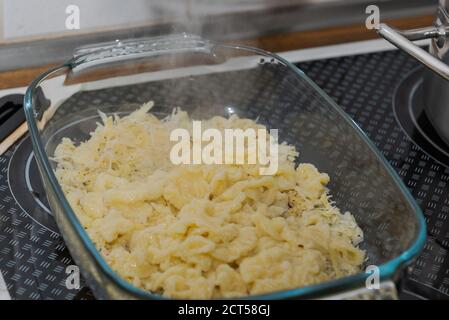 Casseruola di vetro con Spaetzle formaggio, una specialità della germania meridionale fatta di grumi di pasta in piedi sul forno Foto Stock