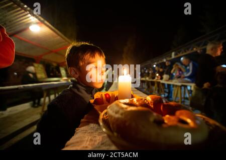 Bambino nella notte di Pasqua con un rotolo e una candela nel cortile. Foto Stock