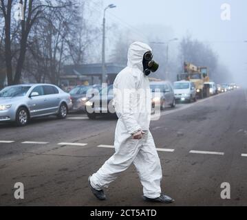 Lunghezza completa di ecologist in copriscarpe che cammina sulla strada della città con le automobili. Ambientalista maschile con tuta bianca e maschera a gas. Concetto di ecologia e inquinamento urbano. Foto Stock