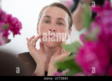 Una donna di mezza età esamina le rughe su uno sfondo di fiori. Cura per la pelle invecchiata. Foto Stock