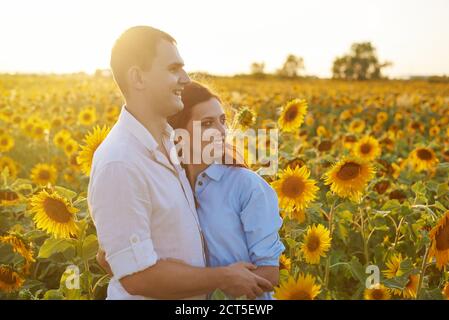 Sorridente coppia felice abbracciando nel mezzo di un campo con girasoli. Abbagliamento da sole. Coppia romantica in un momento d'amore. Foto Stock