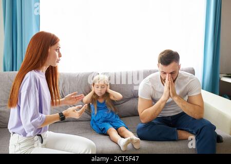 triste e disperata bambina durante la disputa dei genitori, ha intasato le orecchie seduta sul divano a casa, arrabbiato genitori combattendo. preoccupata turbata piccola figlia hur Foto Stock