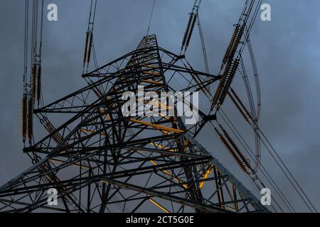 Guardando in su al pilone di elettricità illuminato di sole con cielo di moody a. crepuscolo prima di una tempesta Foto Stock