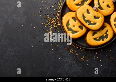 Biscotti di Halloween con pan di zenzero su sfondo nero. Divertenti volti di zucca. Foto Stock