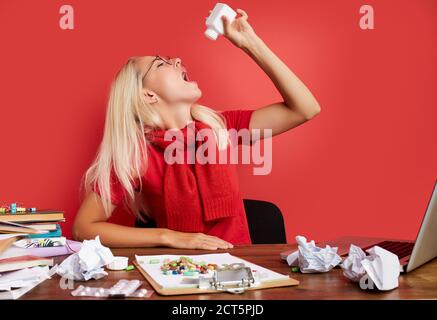 la giovane donna depressa soffre di mal di testa al lavoro, prendere una medicina, un sacco di carte e laptop sul tavolo Foto Stock