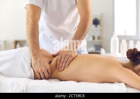 L'osteopata maschile massaggia la schiena di una ragazza sdraiata su un divano in un ufficio luminoso. Foto Stock