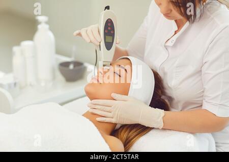 Donna dermatologa che fa l'apparecchio di ultrasuoni pulizia del viso per la donna giovane Foto Stock