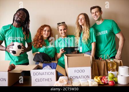 diversi volontari si impacchettano, raccolgono aiuti umanitari in una scatola di donazione. gruppo multietnico di persone che lavorano in fondazione caritatevole aiutando in cris Foto Stock