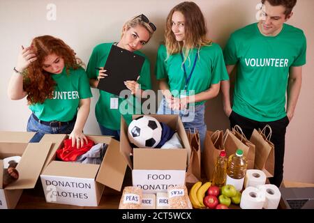 diversi volontari si impacchettano, raccolgono aiuti umanitari in una scatola di donazione. gruppo multietnico di persone che lavorano in fondazione caritatevole aiutando in cris Foto Stock