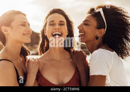 Primo piano di tre donne multietniche in piedi insieme all'aperto. Amici felici in una vacanza in piedi insieme e ridendo. Foto Stock