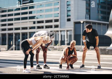 Street runner multietnici che fanno una pausa dopo l'allenamento all'aperto. gruppo fitness riposante e sorridente dopo l'esercizio in città Foto Stock