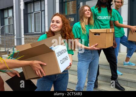 amichevole gruppo di beneficenza interrazziale impegnato in volontario, si levano in piedi all'aperto su scale trasfere scatole con cibo e vestiti, concetto di donazione Foto Stock