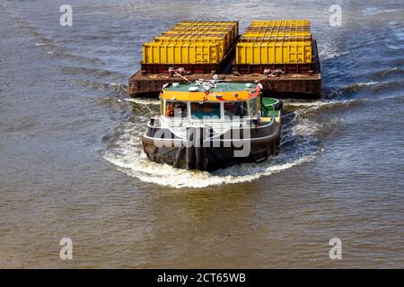 Rimorchiatore barca che tira il trasporto come contenitori in un grande separato Chiatta lungo il Tamigi a Londra Foto Stock