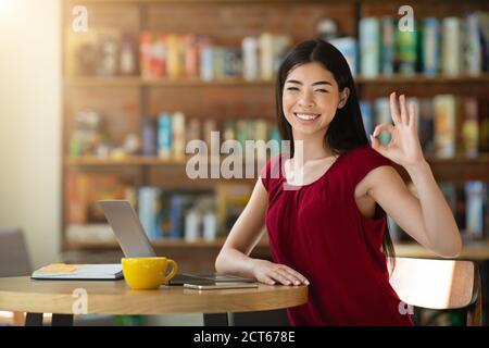 Opportunità di business in remoto. Happy Korean Freelancer Donna mostrando OK Accedi Cafe Foto Stock