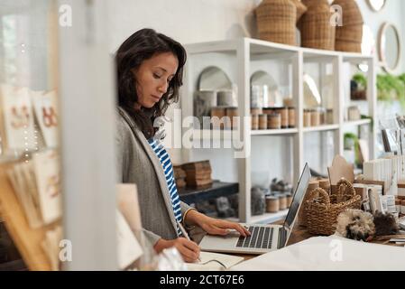 Giovane donna asiatica che lavora dietro il bancone del suo negozio Foto Stock
