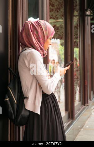 London West End Knightsbridge Street scena araba musulmana donna hijab abaya negozio vetrina telefono cellulare Foto Stock