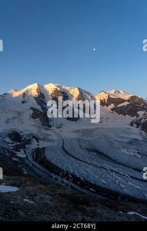 Die ebenfalls dreigipflige Palü und die ebenfalls dreigipflige Bellavista (von links). Davor der Persgletscher. Darüber der Mond. Bei Sonnenaufgang. Obereng Foto Stock