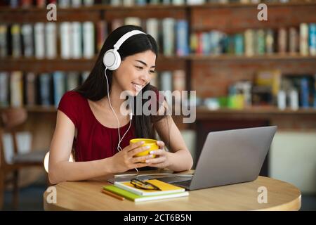 Seminario Web Smiling Asian Woman Watching con laptop e cuffie in Caffè Foto Stock