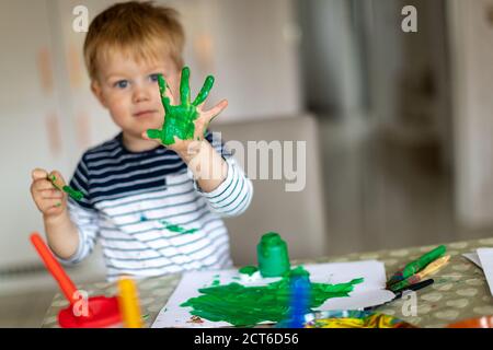 Ragazzo di tre anni occupato pittura a casa, con pentole e pennelli di vernice. Foto Stock