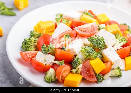 Insalata vegetariana con broccoli, pomodori, formaggio feta e zucca su piastra bianca in ceramica su fondo grigio in cemento e tessuto di lino, vista laterale, Foto Stock