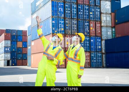 Il tecnico o il tecnico che indossa una maschera protettiva per proteggerla Covid-19 discussione e parlare per ispezione a container cargo, Business lo Foto Stock