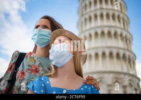 Viaggio durante la pandemia del coronavirus. Giovani turisti di madre e figlia con maschere mediche che guardano in lontananza vicino alla torre pendente a Pisa, Italia. Foto Stock