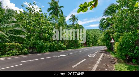 Moorea paesaggio con una strada asfaltata vuota e un segnale di avvertimento rosso con una doppia curva. Foto Stock