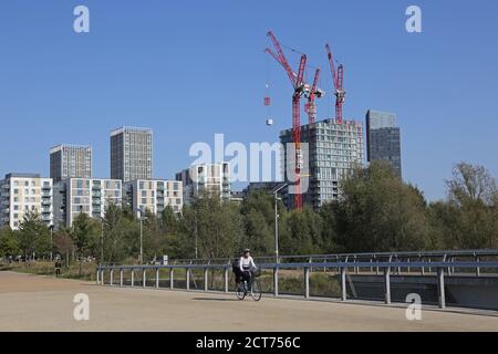 Queen Elizabeth Olympic Park, Londra. Ciclisti sul ponte di East Cross. Gru oltre come più blocchi di appartamenti sono aggiunti al sito Olympic Village. Foto Stock