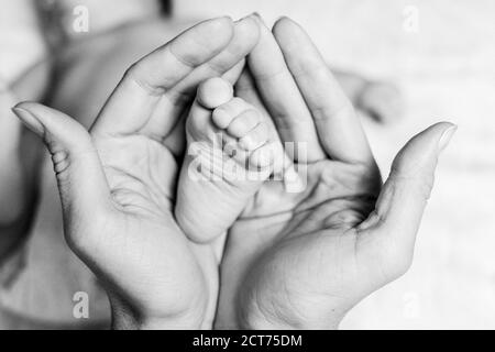 La madre tiene il piede del bambino nelle sue mani. Primo piano delle mani. Foto in bianco e nero. Concetto di maternità e di giorno dei bambini. Foto Stock