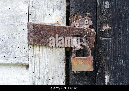 Lucchetto arrugginito su una vecchia porta di legno con vernice sfaldante. REGNO UNITO. Foto Stock