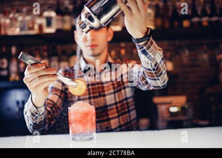 Il barman mescola uno spettacolo di cocktail rossi con un colorato banco bar alcolico Foto Stock