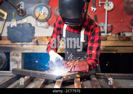 Saldatrice industriale con maschera protettiva e utensile a punta lavora in fabbrica. Scintille da alta elettricità Foto Stock