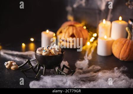 Caramelle e biscotti a forma di occhio per le vacanze di Halloween, sfondo scuro con ciottoli, zucche e candele Foto Stock