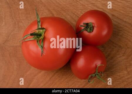 Tre pomodori rossi, uno in più e due più piccoli su una tavola di legno Foto Stock