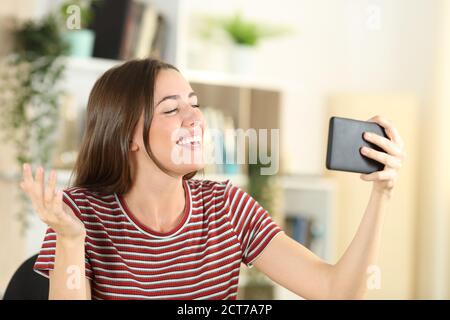 Felice teen che parla in una videochiamata su smartphone seduto a casa Foto Stock