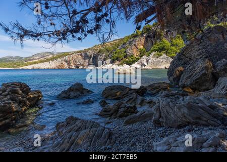 Incredibile natura dell'isola di Hvar con ripide scogliere rocciose che si innalzano sull'appartata spiaggia 'Zarace', circondata da turchese, mare adriatico Foto Stock
