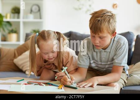 Ritratto della ragazza bionda carina con la sindrome di Down disegno insieme con il fratello maggiore a casa, copia spazio Foto Stock