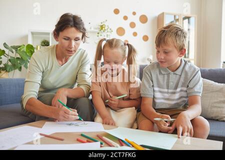 Ritratto di ragazza bionda carina con la sindrome di Down ridendo felice mentre si cofigura con madre e fratello a casa Foto Stock