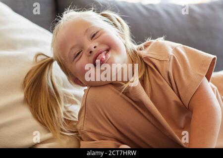 Ritratto di bambina spensierata con la sindrome di Down che aderisce alla lingua fuori mentre grimacing per la macchina fotografica Foto Stock