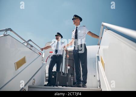 Due senior handsome pilota con borsa a rotolamento che va a casa dopo volo lungo Foto Stock